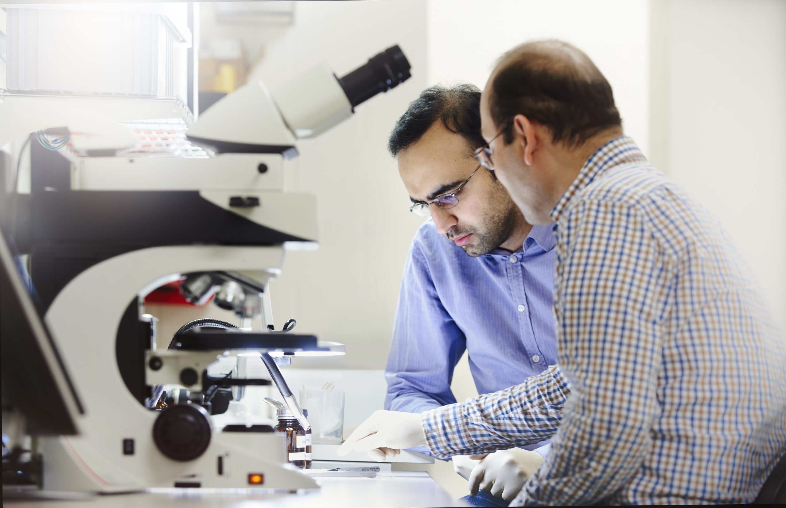 2 people working in a lab in front of a microscope